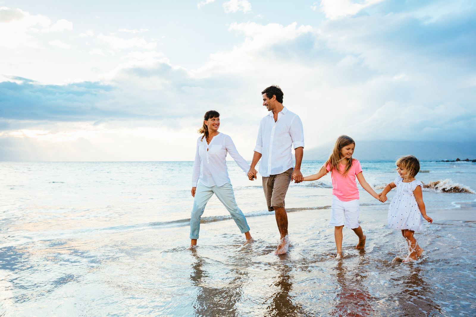 A young family holding hands and walking along the beach